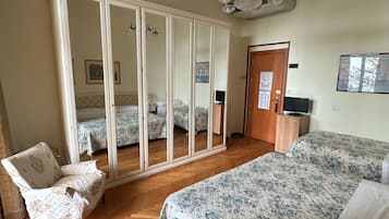 Un dormitorio con un armario grande, una cama con ropa de cama floral, una silla y un escritorio con un control remoto.