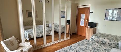 Un dormitorio con un armario grande, una cama con ropa de cama floral, una silla y un escritorio con un control remoto.
