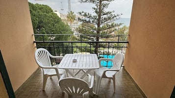 A balcony with a table and chairs, a view of the sea, a crane, and a tree.
