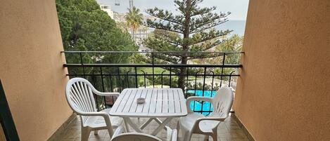 Un balcón con mesa y sillas, vista al mar, una grúa y un árbol.
