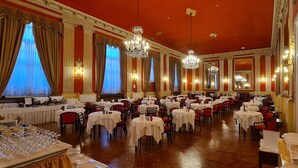 Un amplio comedor con numerosas mesas, candelabros y paredes rojas.