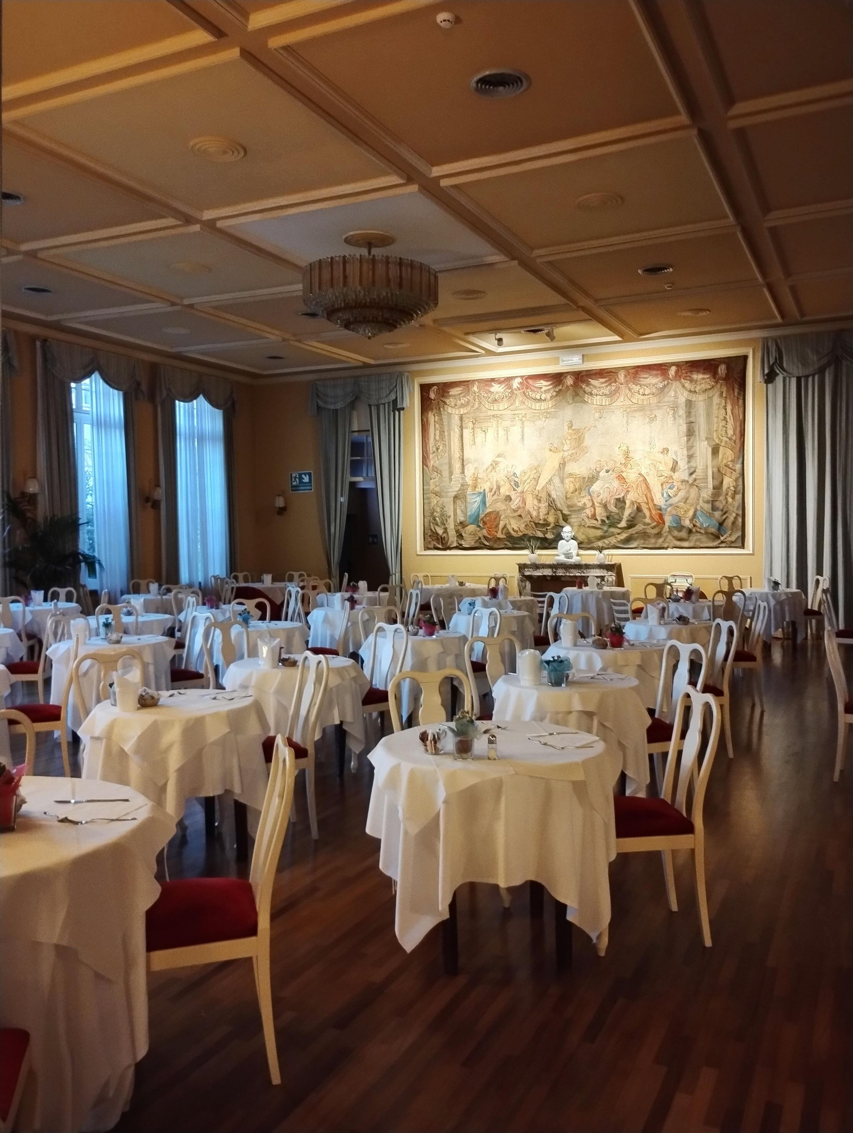 A banquet hall with round tables, chairs, and a large wall mural.