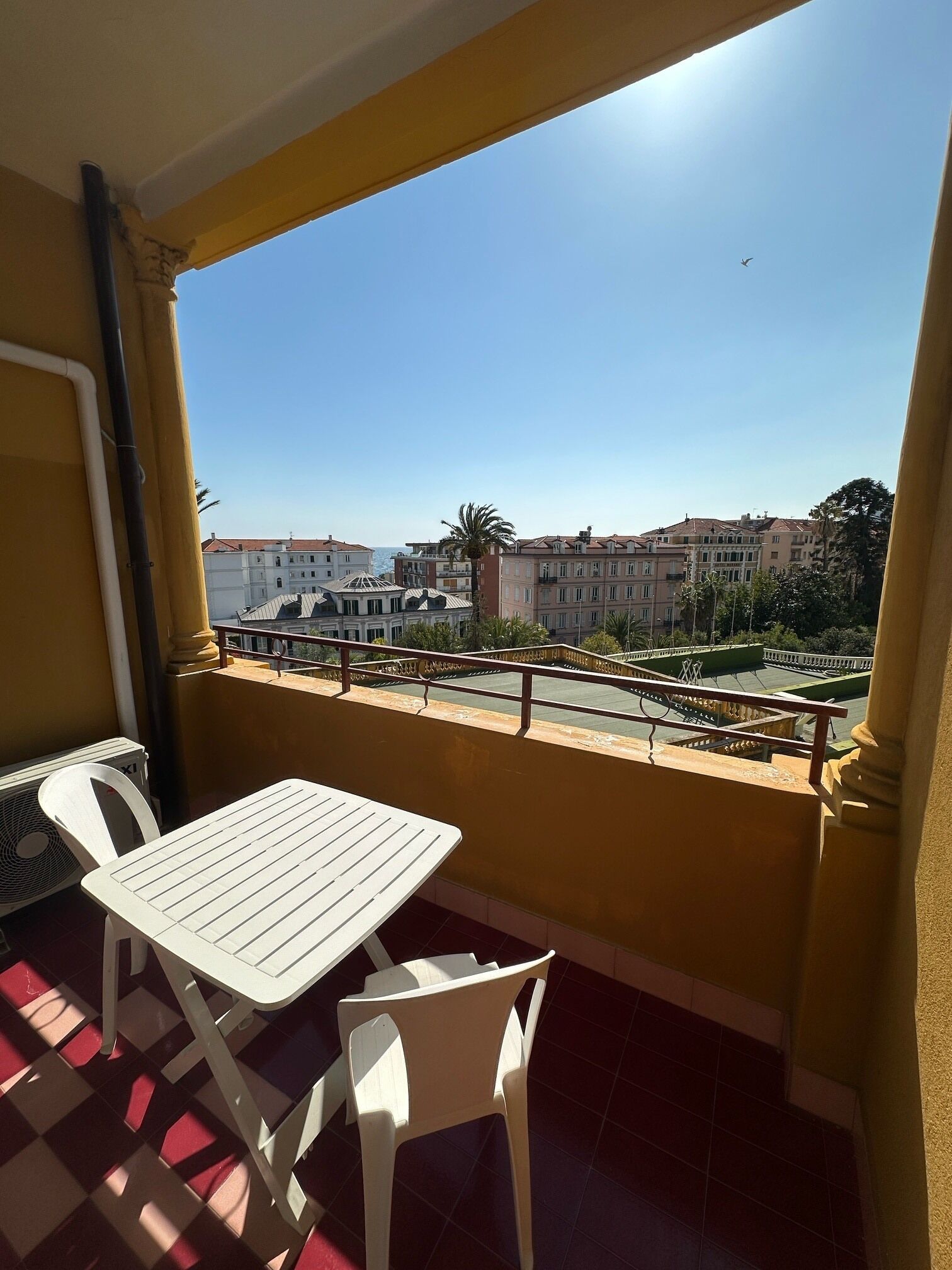 A balcony with a table and chairs, overlooking a cityscape with buildings and a clear sky.