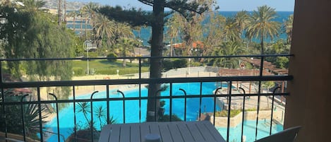 Un balcón con mesa y sillas, con vista a una piscina y al mar.