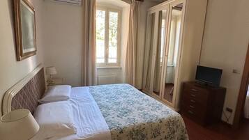 A hotel room with a bed, a desk with a lamp, a TV on a dresser, and a window with curtains.