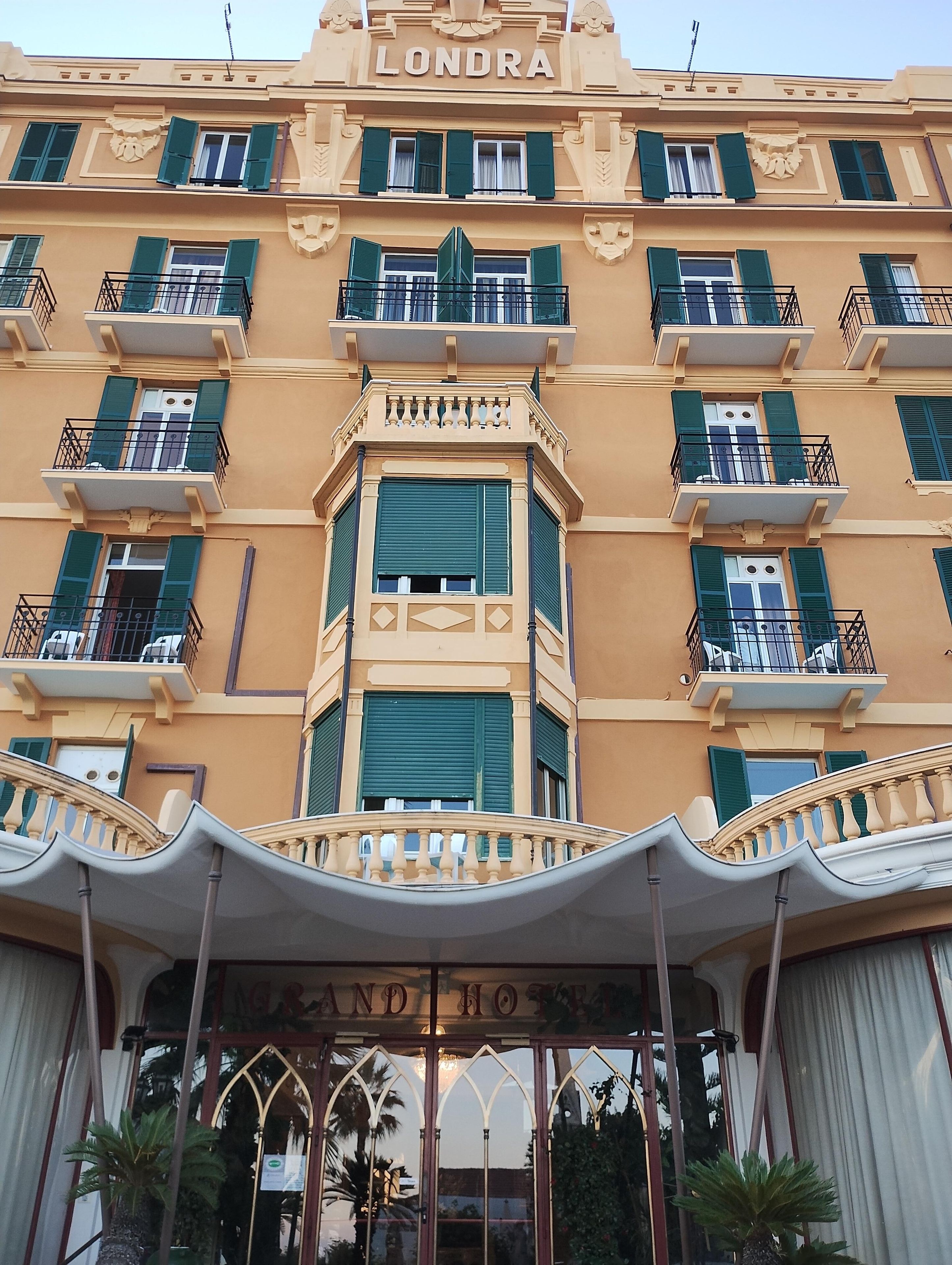 Un hotel a più piani con balconi, un ingresso centrale e un cartello con scritto 'LONDRA GRAND HOTEL'.