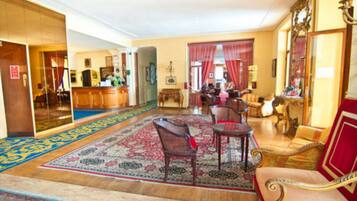 Eine geräumige Lobby mit großem Teppich, Holzmöbeln und einem roten Vorhang.