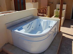 Ein Whirlpool in einer Außenanlage mit Holzlattenzaun und Pflanzgefäß mit Pflanzen.