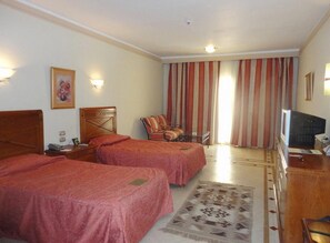 A hotel room with two beds, a desk, a chair, a television, and a window with curtains. - Imperial Shams Abu Soma (Safaga)