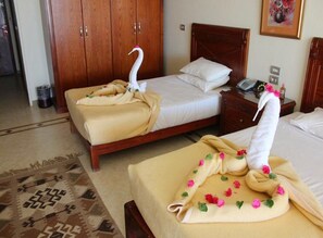 A hotel room with two beds, wooden headboards, a bedside table with a phone, and a wall-mounted painting. - Imperial Shams Abu Soma (Safaga)
