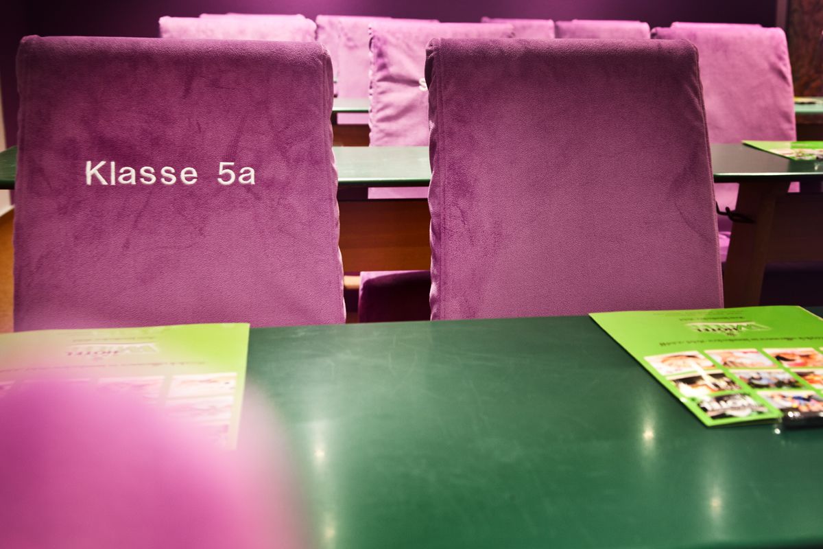 Ein Klassenzimmer mit violetten Stühlen, beschriftet mit 'Klasse 5a', und grünen Tischen.
