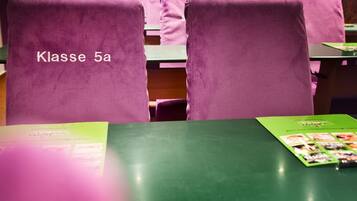 Ein Klassenzimmer mit violetten Stühlen, beschriftet mit 'Klasse 5a', und grünen Tischen.