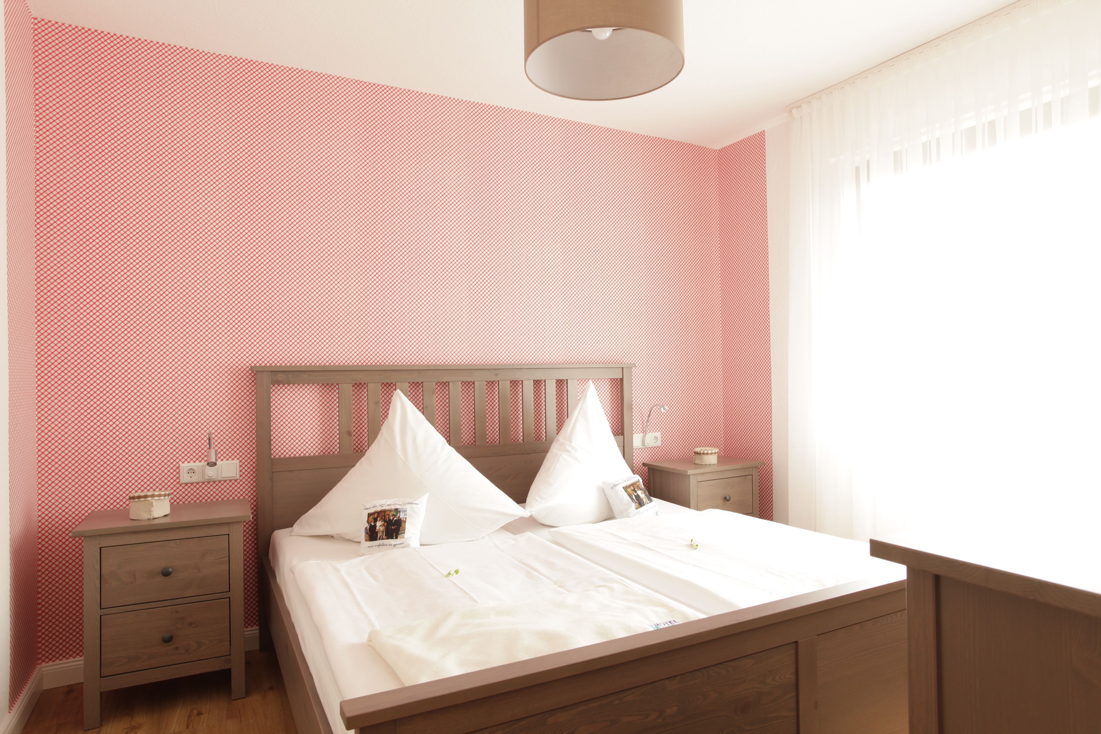 A neatly made bed with white linens and pillows, a wooden headboard, and a nightstand with a lamp and a small table beside it.