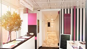 A reception area with a sign reading "Reception Hotel & Spa," a reception desk with a vase of flowers, and a hallway with striped curtains. - Hotel Wulff (Bad Sassendorf)