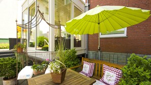 A wooden table with a bench, a green umbrella, and potted plants. - Hotel Wulff (Bad Sassendorf)