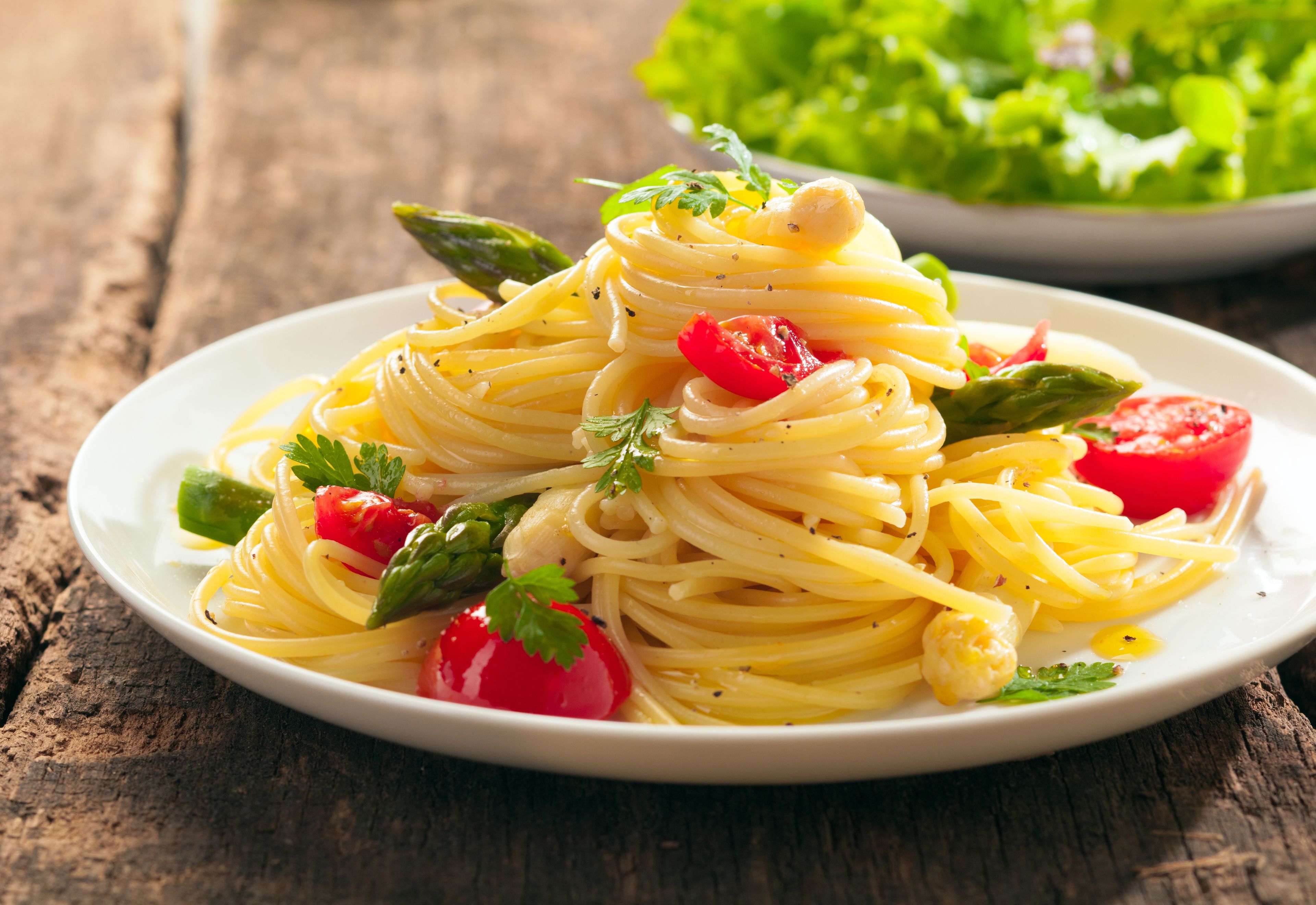 Eine Spaghetti-Kiefer mit Kirschtomaten und Spargel auf einem Holztisch.