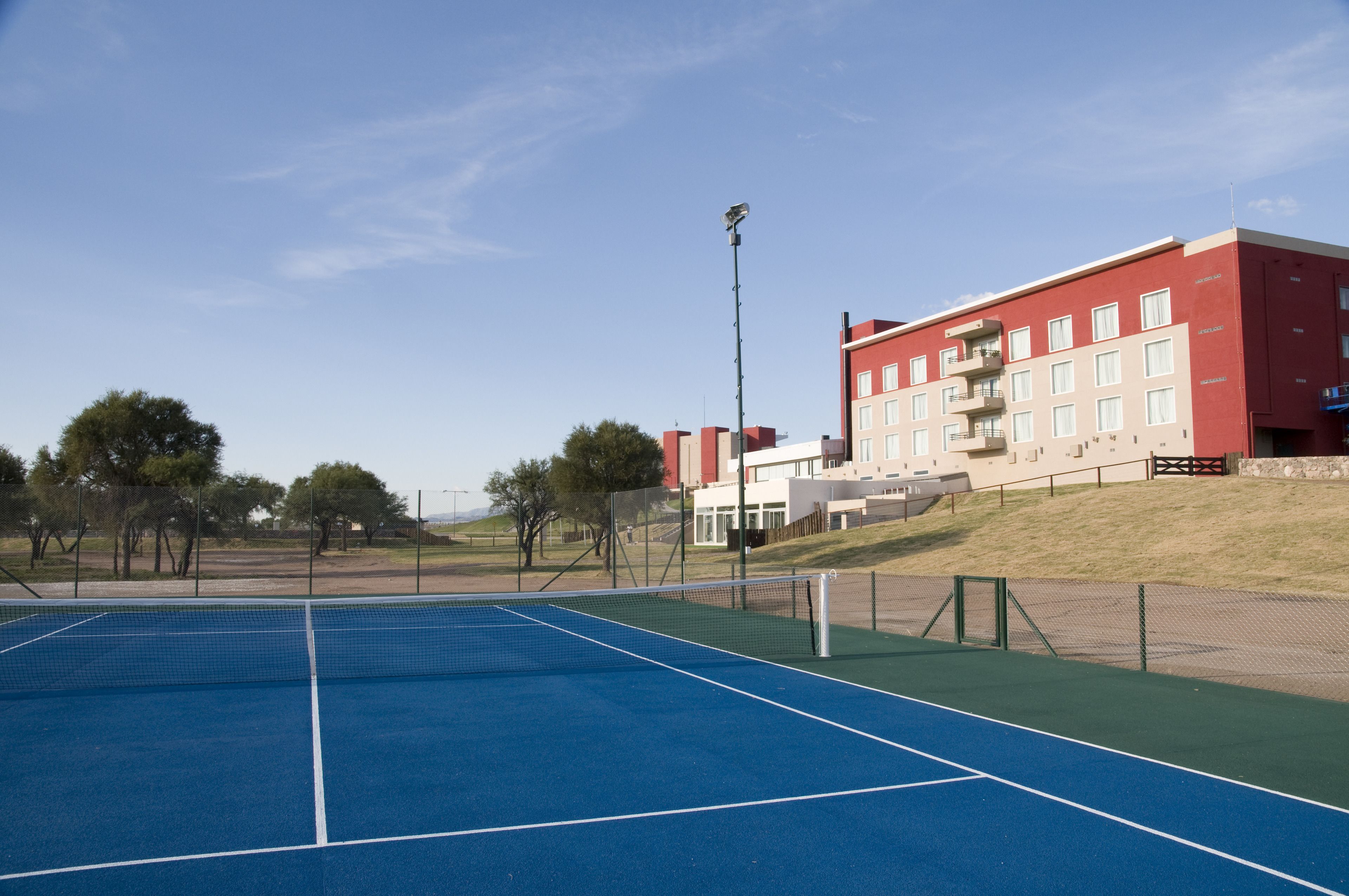 An outdoor tennis court with a net, surrounded by a fence and trees.