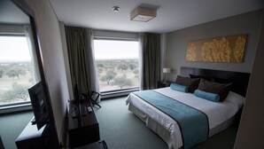 A hotel room with a large bed, a desk with a computer, a TV, and a view of the outdoors. - Epic Hotel San Luis (La Punta)