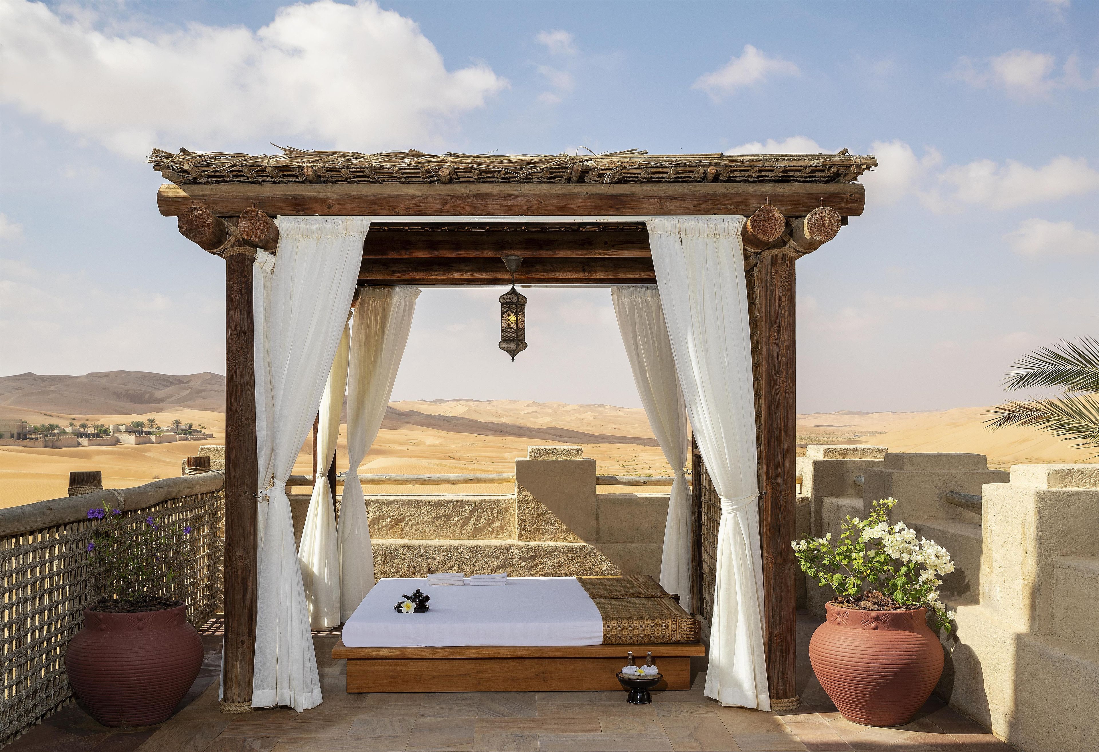 A bed with a white sheet and a hanging lantern, set against a desert landscape.