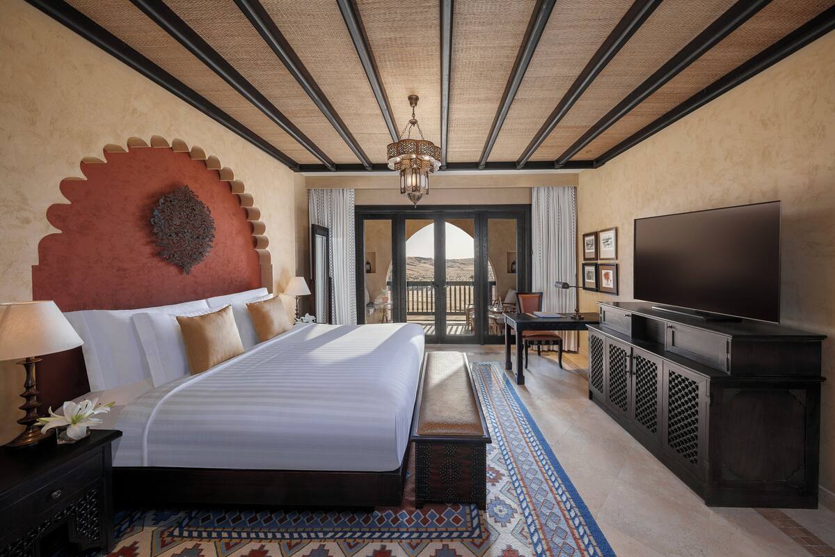 A hotel room with a large bed, a TV, a balcony, and a view of the desert.