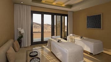 A hotel room with two beds, a sofa, a large window with a view of sand dunes, and a decorative wall piece.