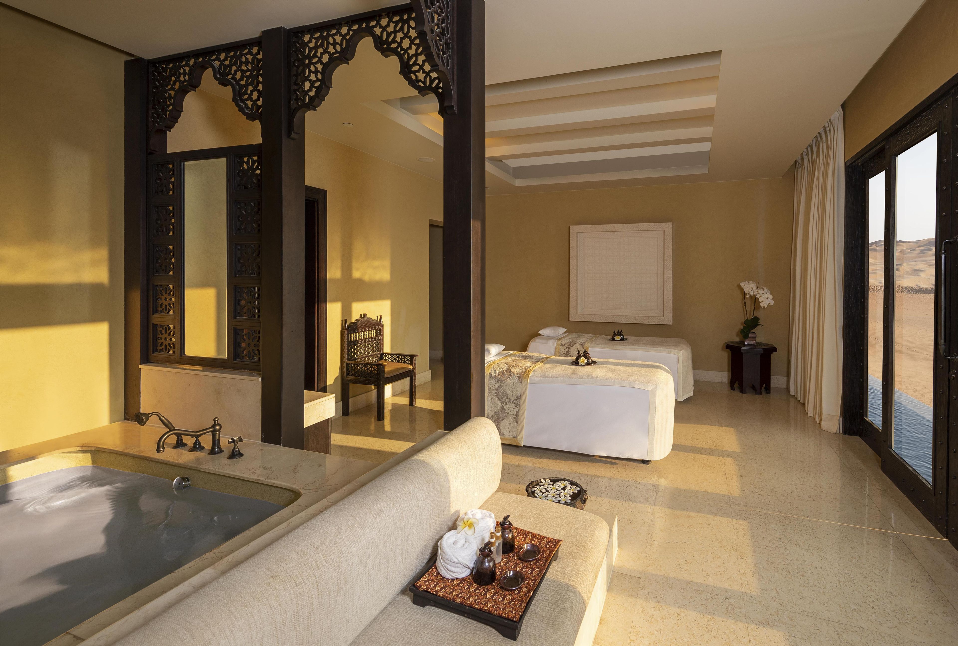 Une chambre d’hôtel avec une grande baignoire, deux lits, un coin salon et une vue sur le désert.