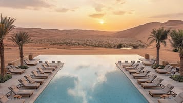 Una piscina al aire libre, sombrillas, sillones reclinables de piscina