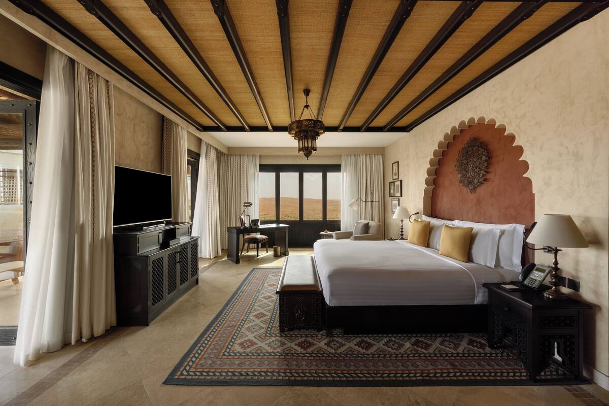 A hotel room with a large bed, a television, a desk, and a view of the desert.
