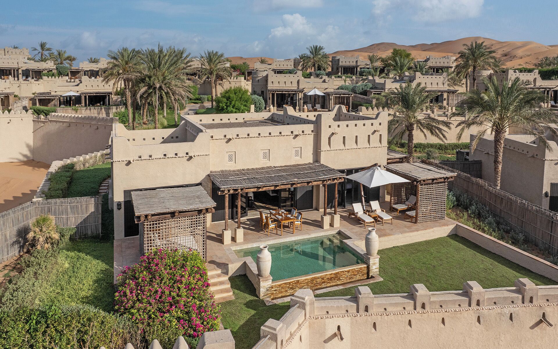 Um resort no deserto com piscina, área de estar externa e palmeiras.