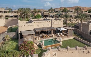 Ein Wüstenresort mit Pool, Sitzgelegenheiten im Freien und Palmen.