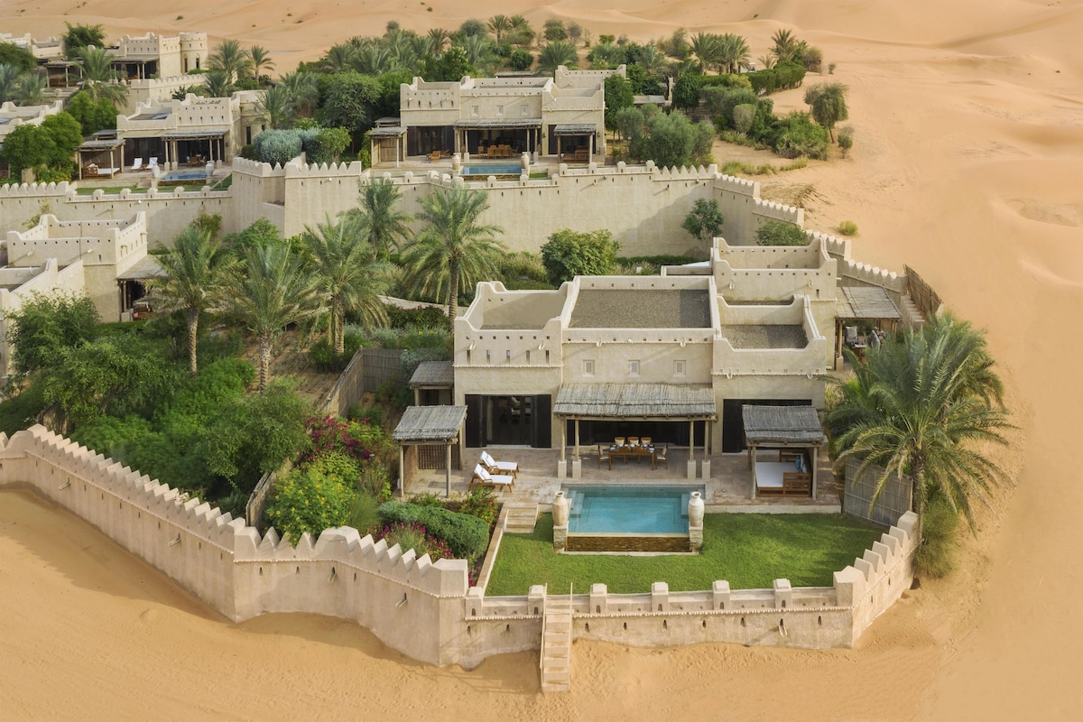 A desert resort with multiple villas, a swimming pool, and lush greenery.
