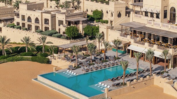 Ett semesterhotell med en pool omgiven av solstolar och palmer.