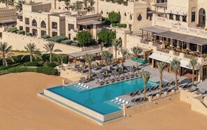 A resort with a swimming pool surrounded by lounge chairs and palm trees. - Qasr Al Sarab Desert Resort by Anantara (Al Mirayr)