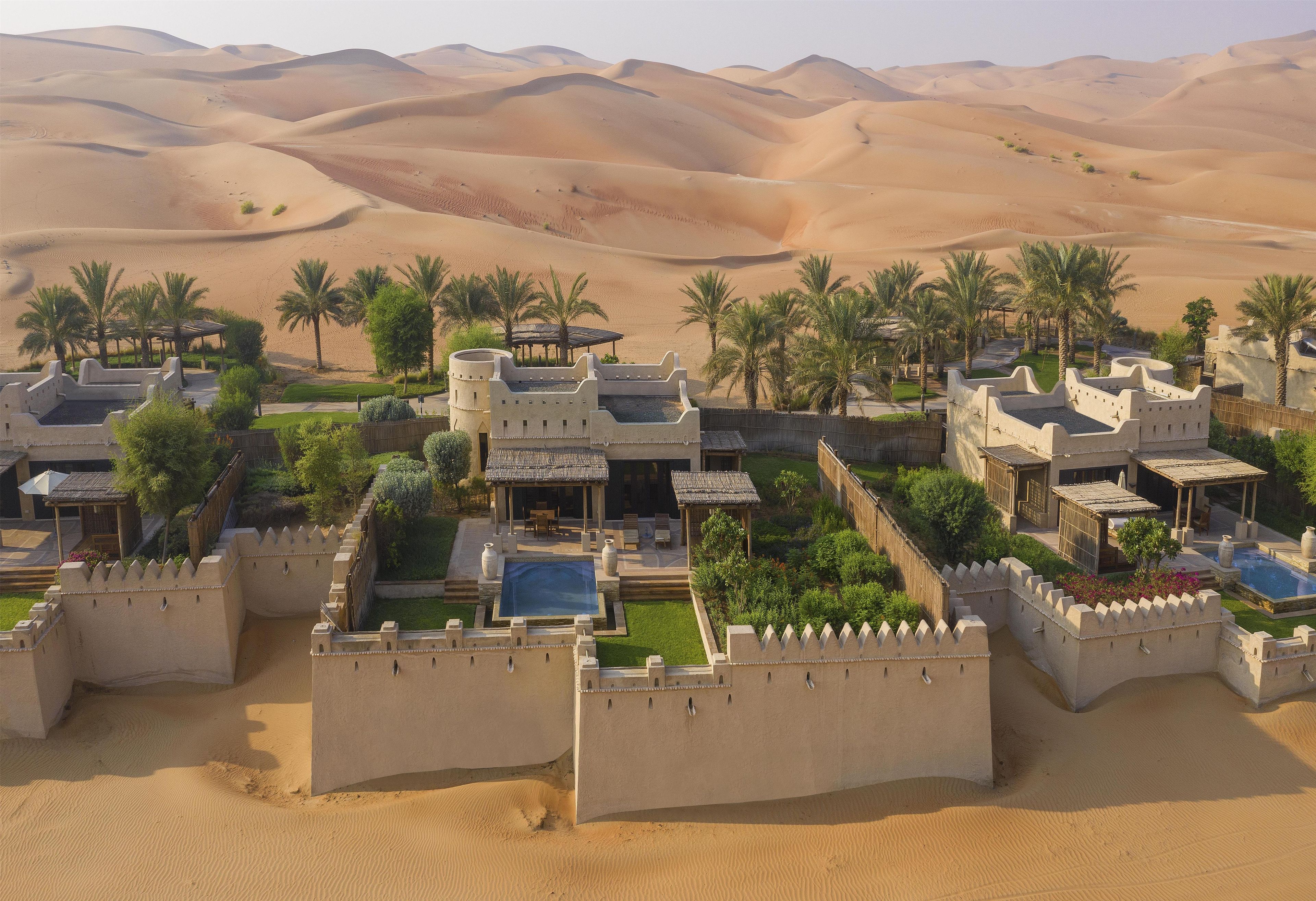 Un complexe hôtelier situé dans le désert, comprenant plusieurs villas, des palmiers et une piscine.