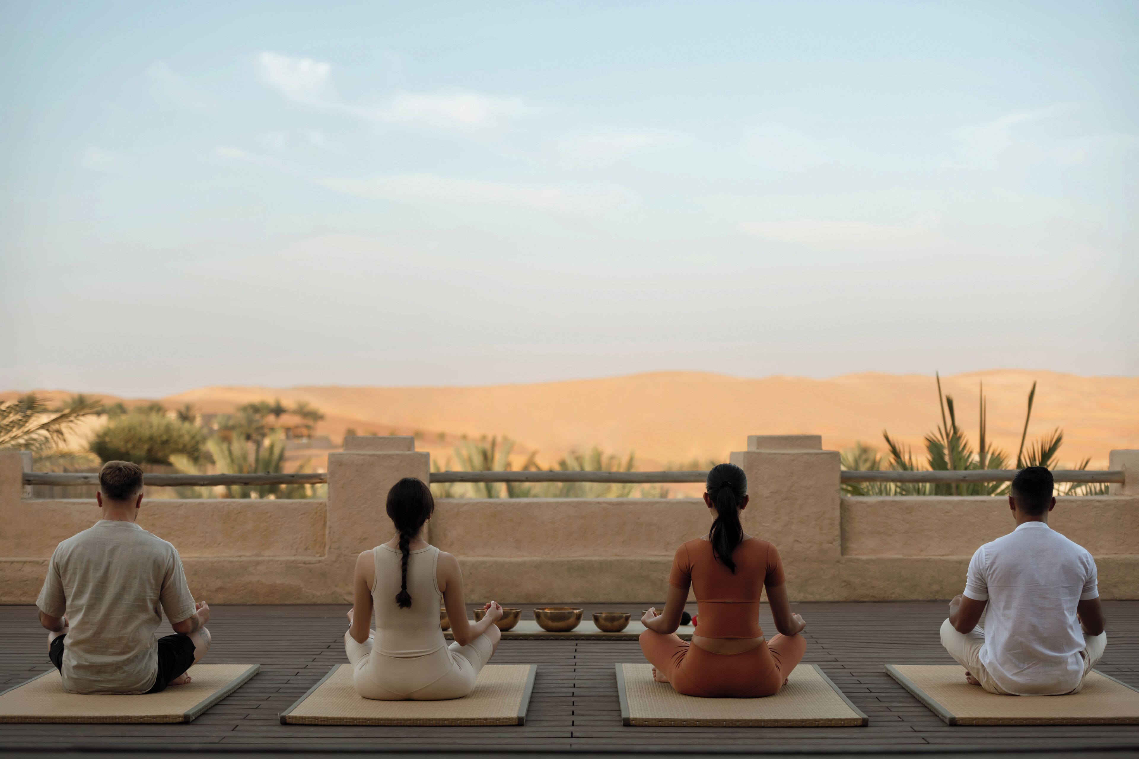 Three people meditating on outdoor mats with a desert landscape in the background.