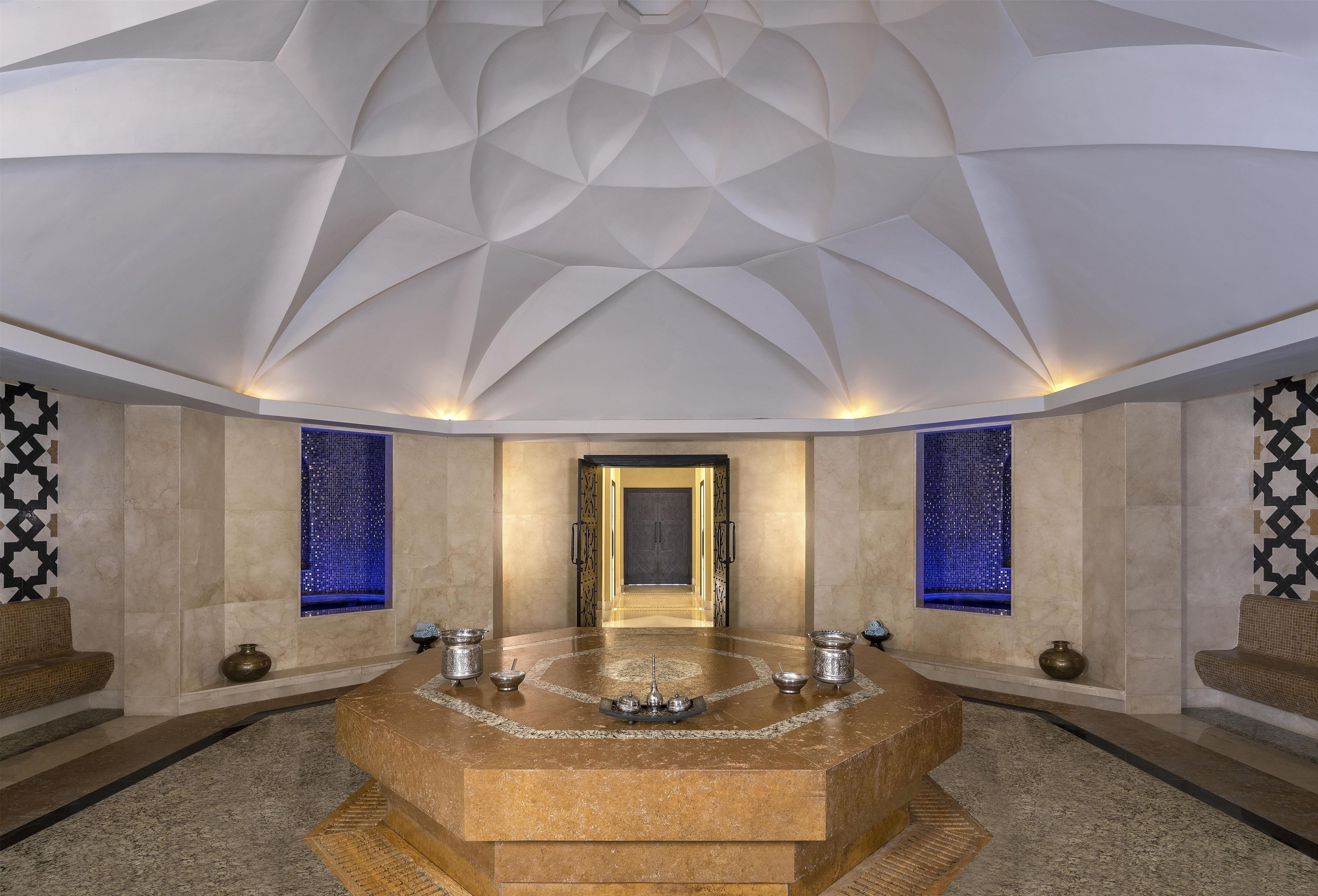 A luxurious bathroom with a central marble sink, two wall-mounted bidets, and a geometric ceiling design.