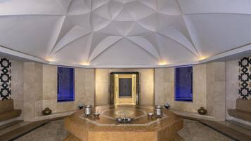 A luxurious bathroom with a central marble sink, two wall-mounted bidets, and a geometric ceiling design.