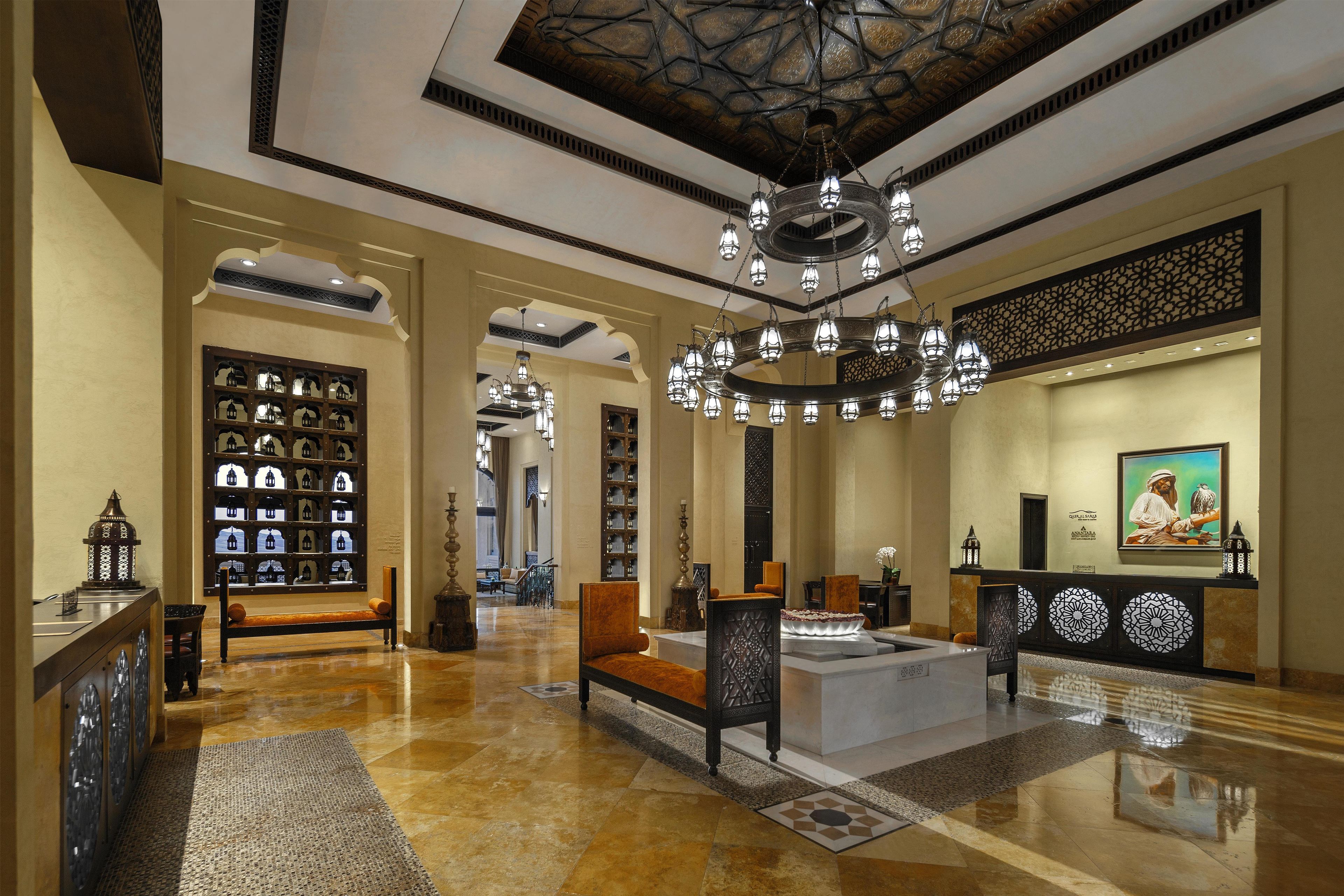 A spacious lobby with a central seating area, a chandelier, and a wall with decorative panels.