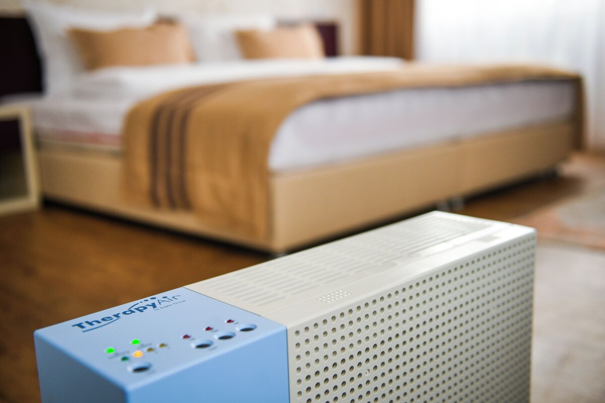 A bedroom with a bed, a bedside table, and a white device on the floor.