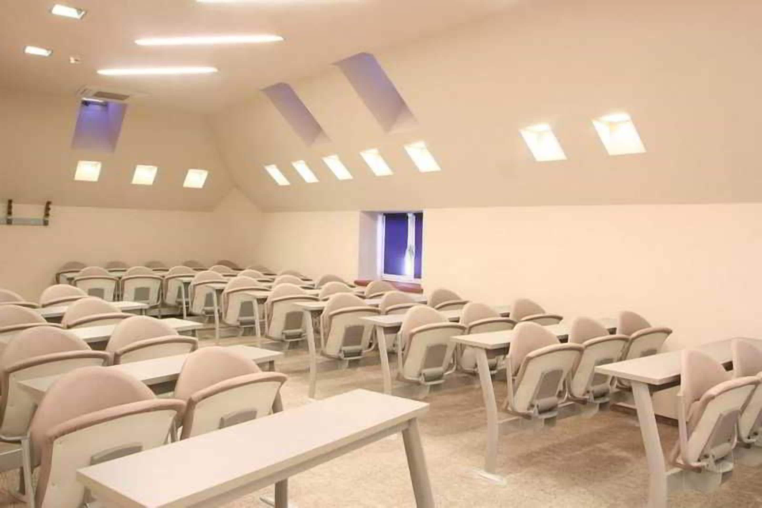 A classroom with rows of desks and chairs, a sloped ceiling with skylights, and a window.