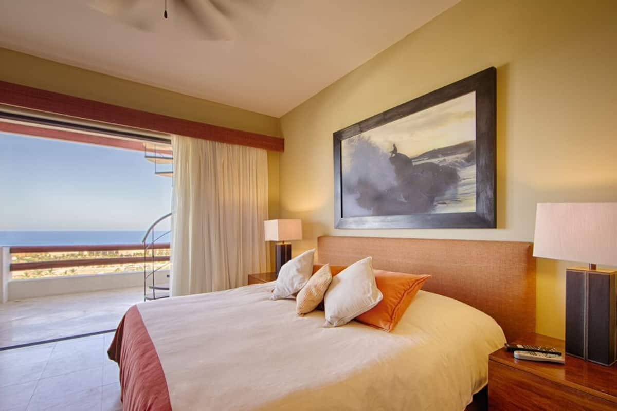 Une chambre d’hôtel avec un grand lit, un tableau au mur, un balcon avec vue et une table de chevet avec une lampe et une télécommande.