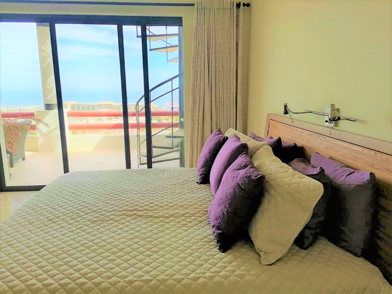 Une chambre à coucher avec un lit, une tête de lit, une fenêtre donnant sur un balcon et un rideau.