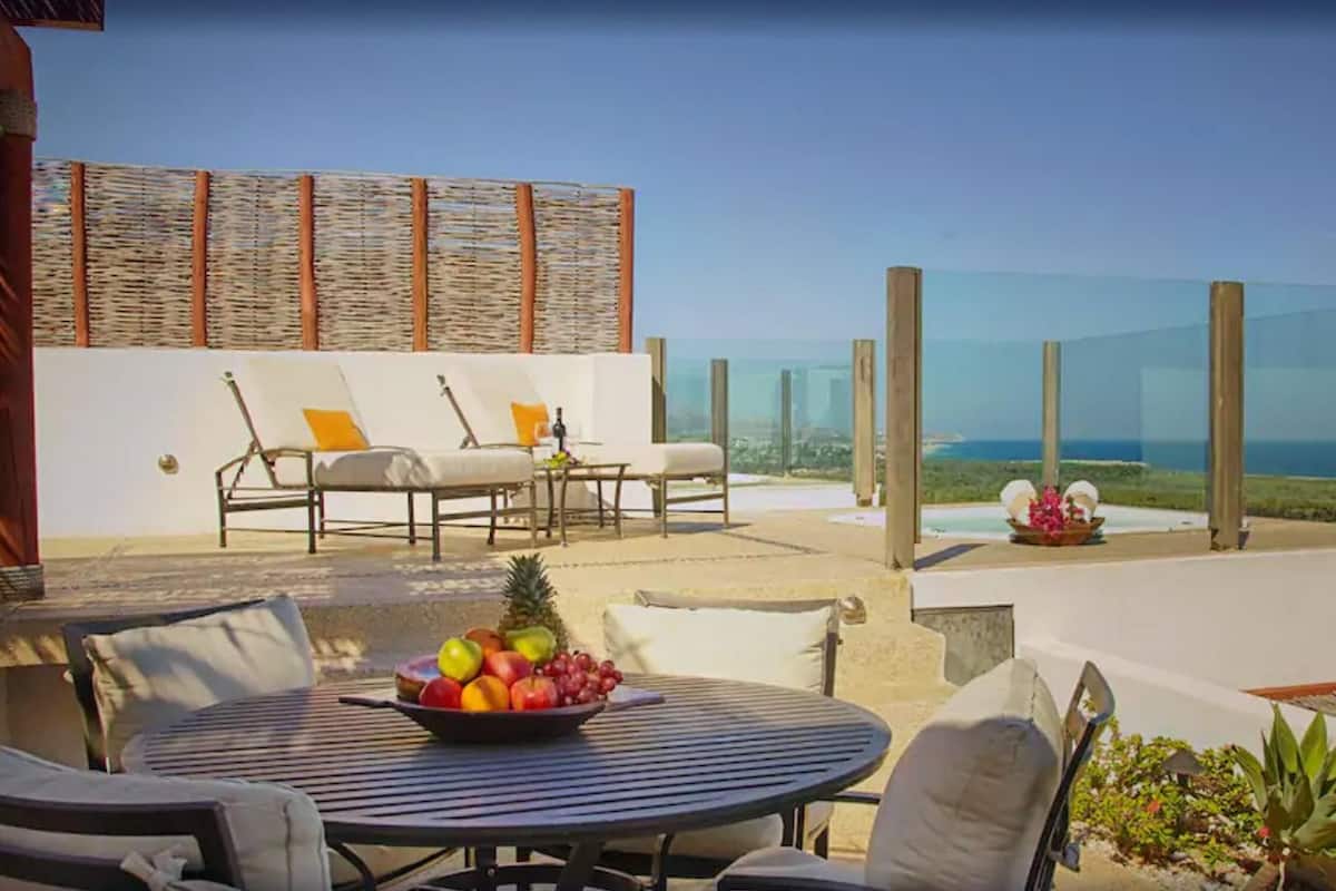 Une terrasse avec des sièges extérieurs, une table garnie de fruits et une vue sur l’océan.