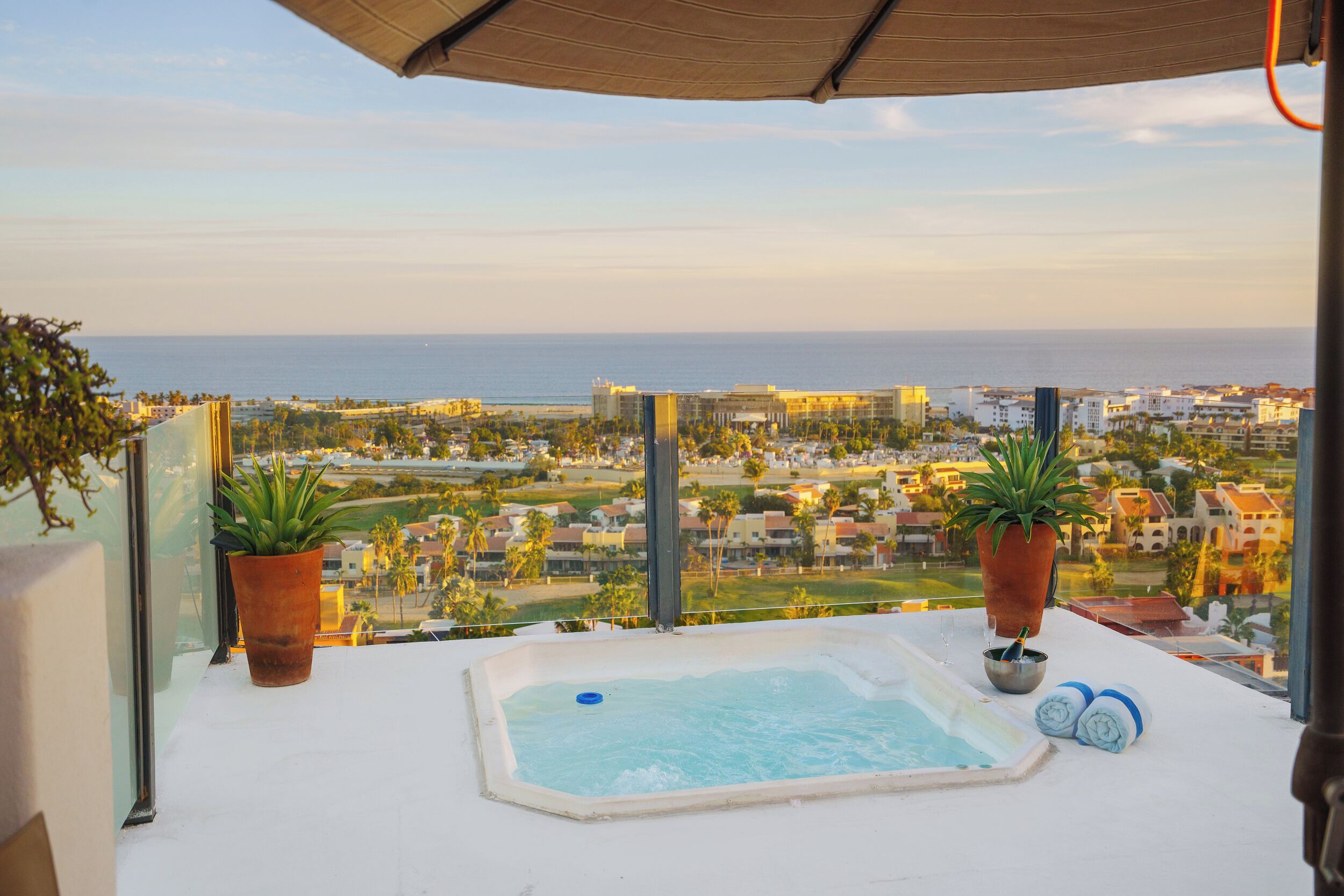 Ein Balkon mit Whirlpool, Topfpflanzen und Blick auf Stadt und Meer.
