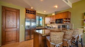 Una cocina con armarios de madera, un refrigerador de acero inoxidable, un microondas y una isla grande con taburetes de bar.