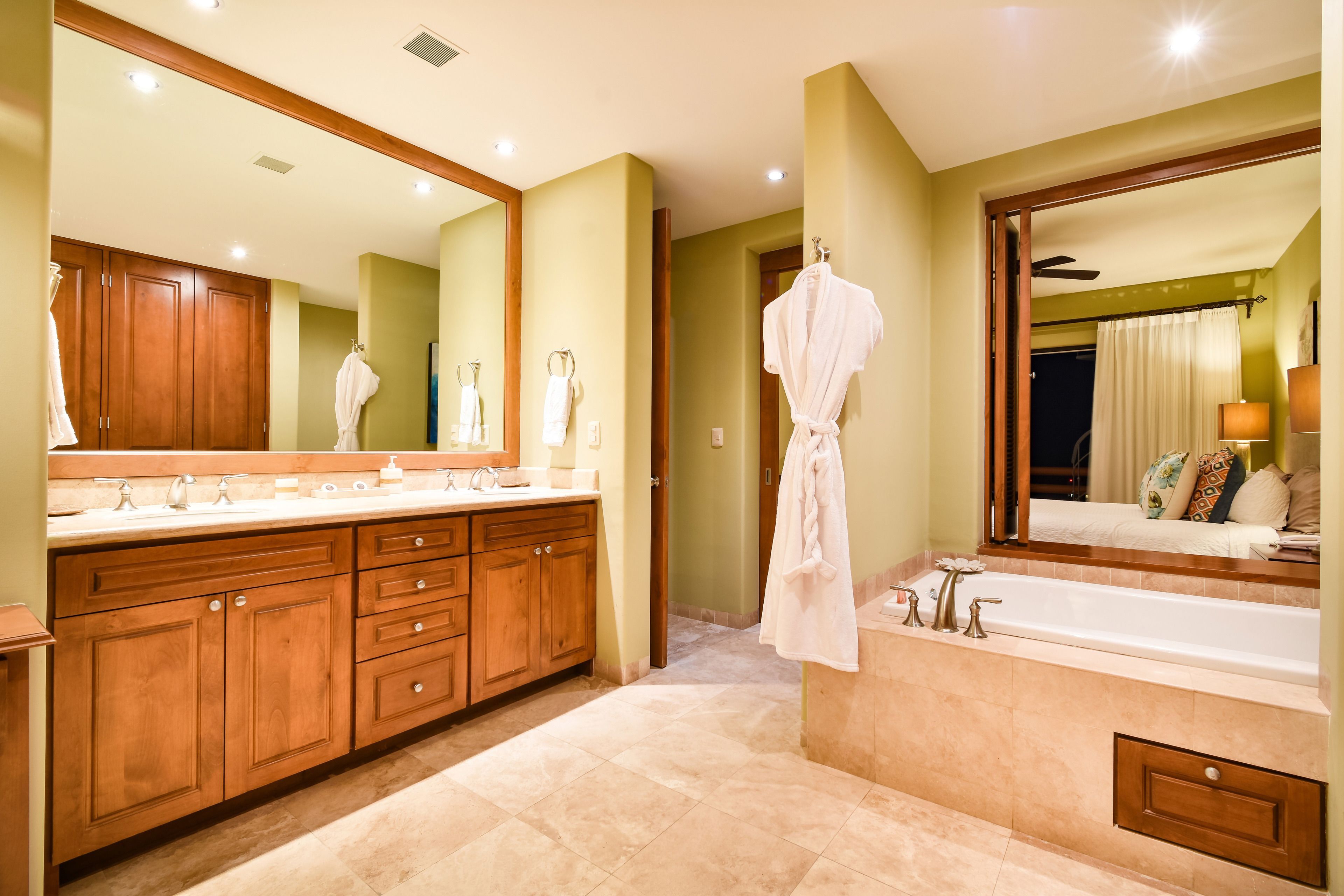 Une salle de bain spacieuse avec un grand miroir, des meubles en bois, une baignoire et un meuble-lavabo avec un évier.