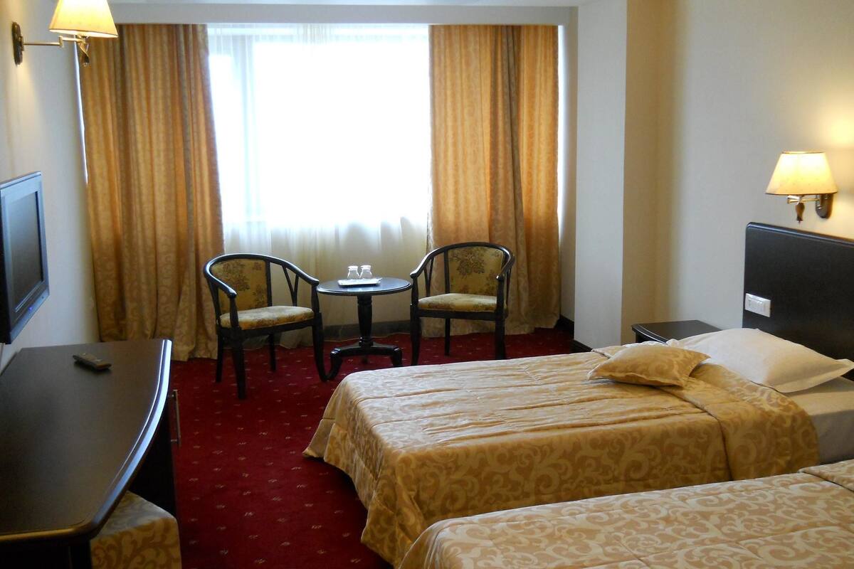 A hotel room with two beds, a desk, a chair, a small table, and a TV.