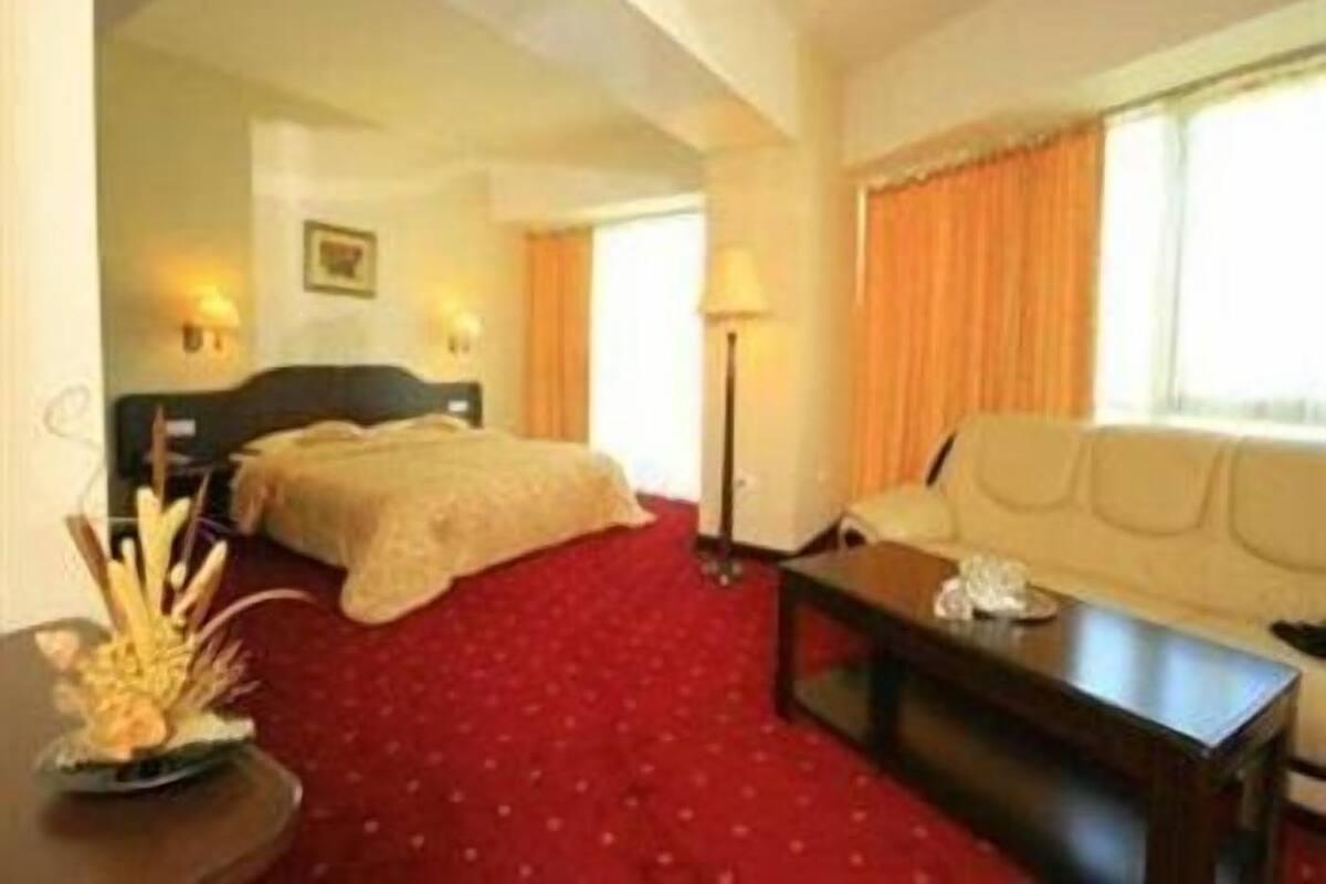A hotel room with a bed, a sofa, a table, and a lamp.