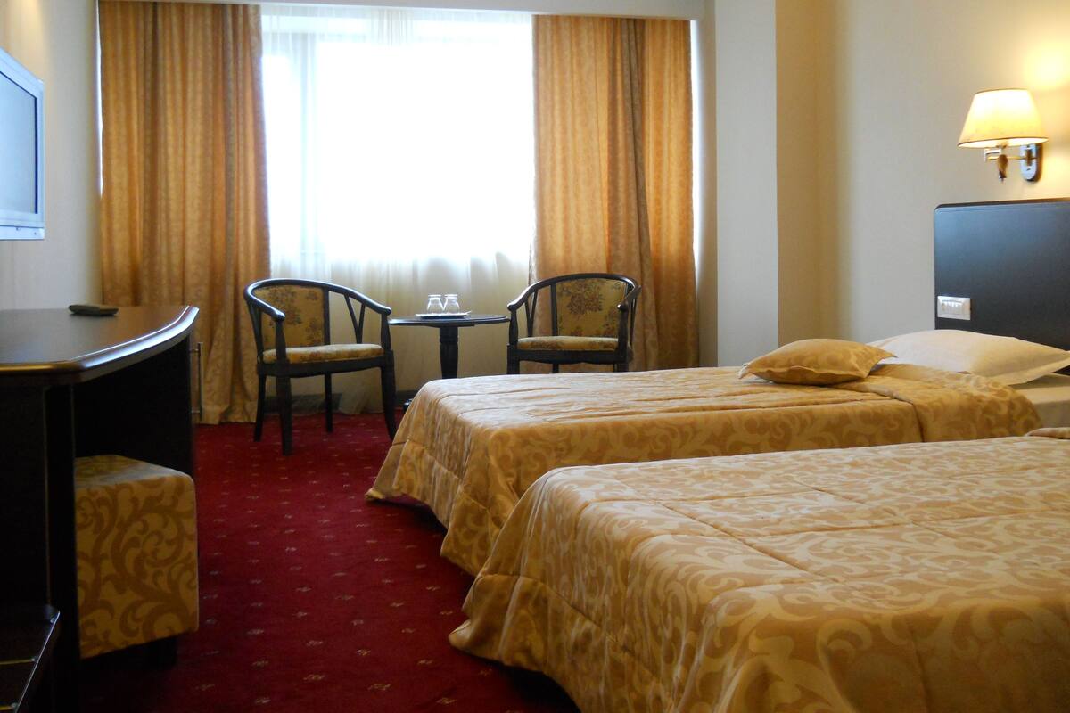 A hotel room with two beds, a desk, a chair, and a TV.