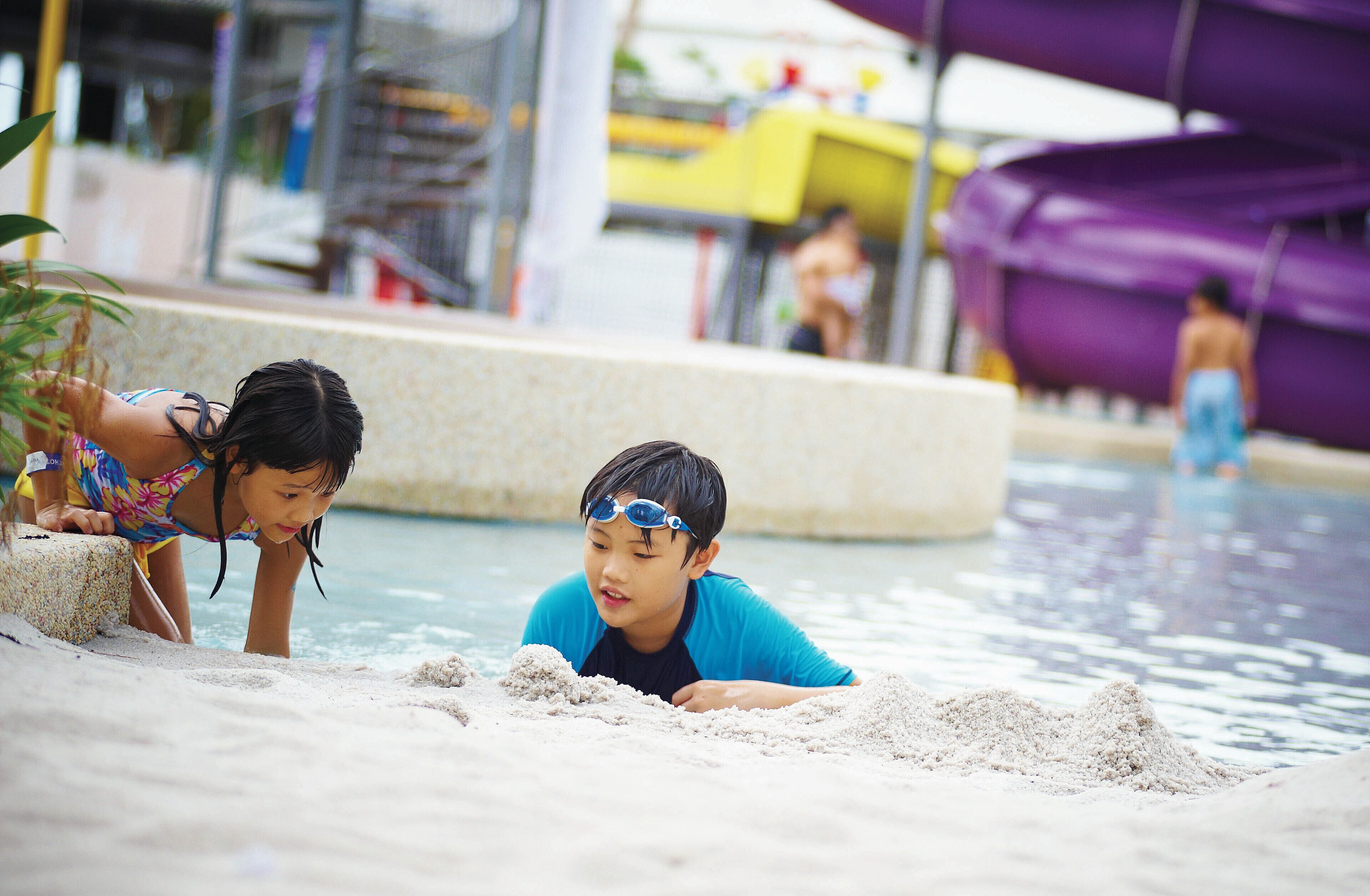 Two children playing with sand by a poolside.